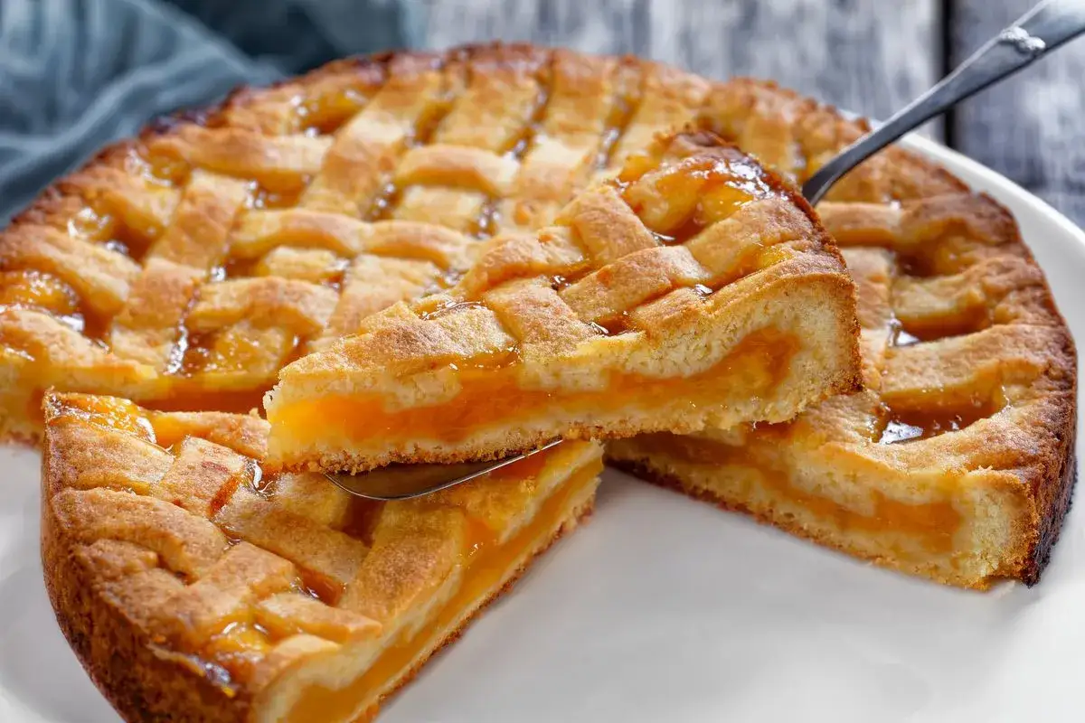 Deliziosa crostata senza glutine con ripieno di albicocche, la fetta sollevata mostra la friabile pasta frolla e la succosa marmellata.