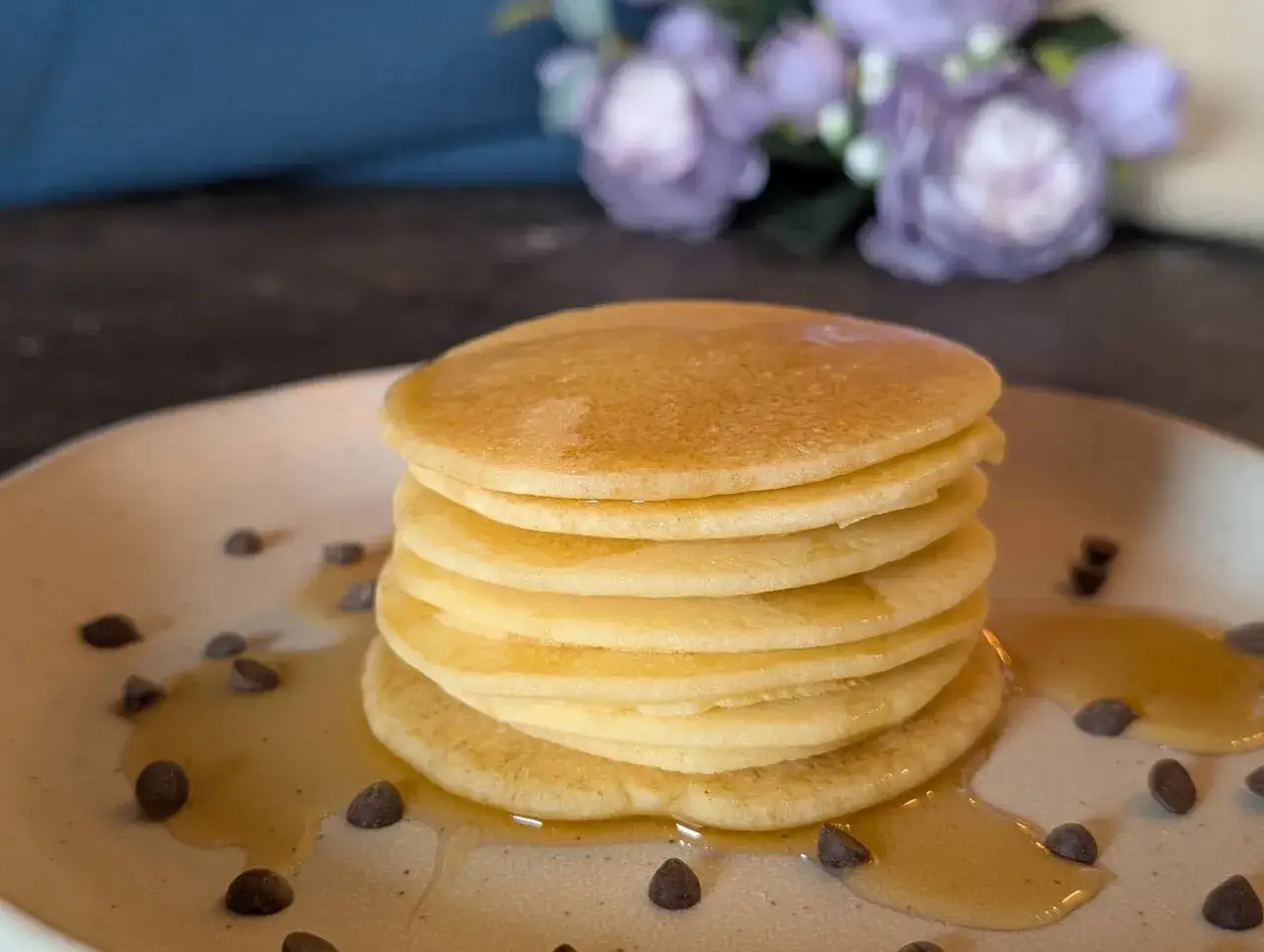Pila di soffici pancake senza glutine e lattosio, inzuppati nello sciroppo e cosparsi di gocce di cioccolato.