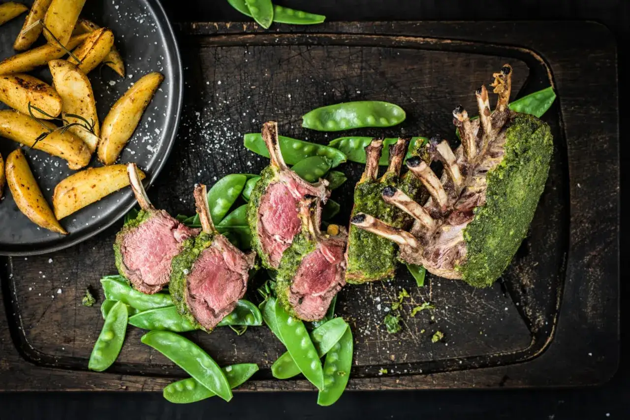 Carr&egrave; di agnello succulento, cotto alla perfezione e ricoperto da un'erba aromatica verde brillante, servito con piselli dolci e patate arrosto croccanti.