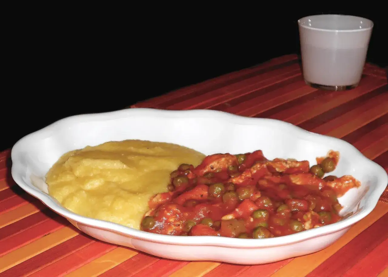 Un invitante spezzatino con piselli, servito su un letto di polenta cremosa, pronto per essere gustato.