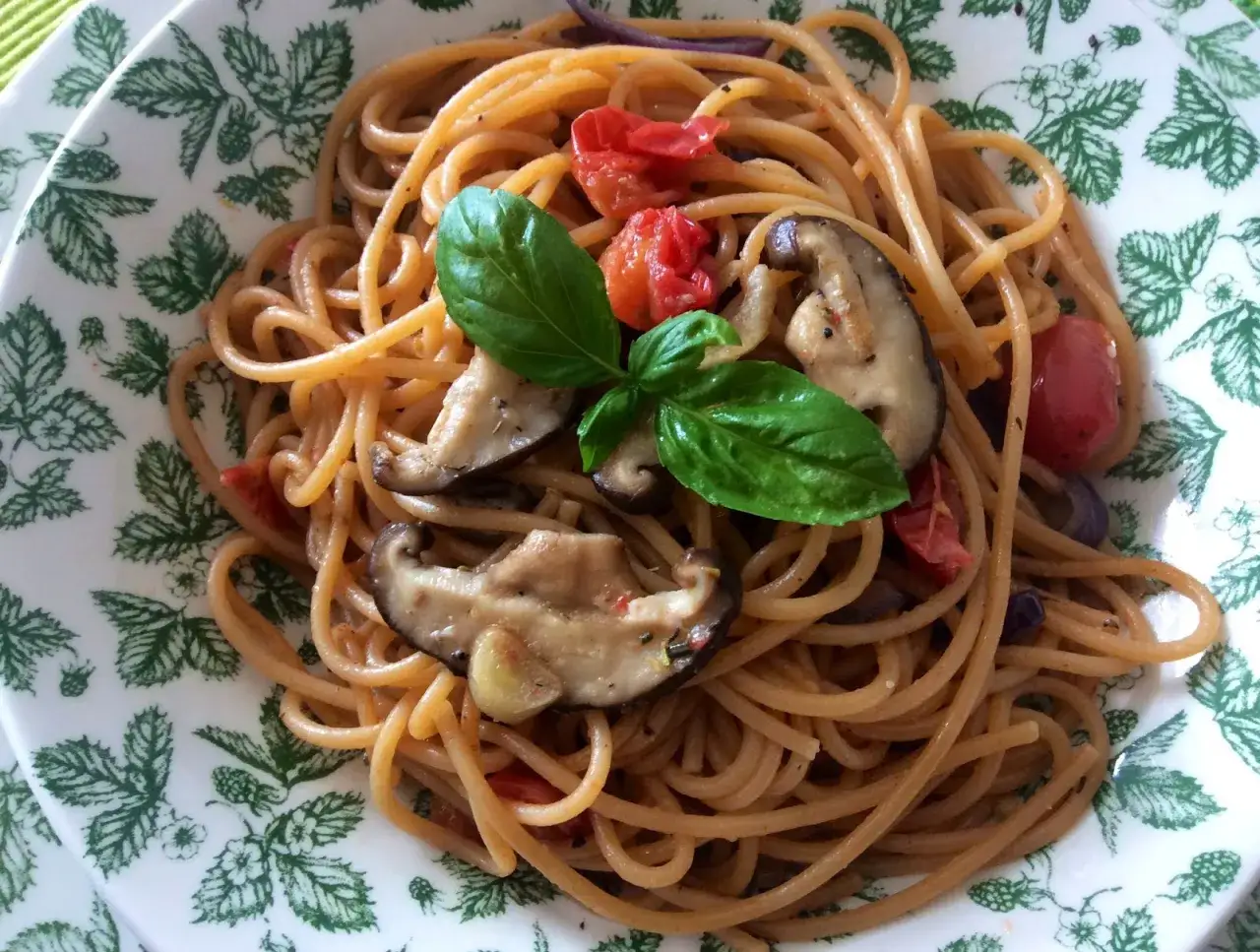 Spaghetti con aglio, olio e peperoncino, funghi shiitake, pomodorini e basilico su un piatto decorato.