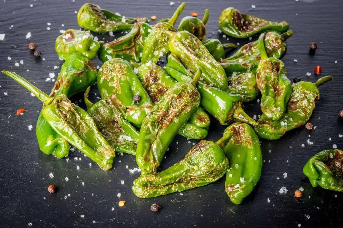 Friggitelli cotti in friggitrice ad aria, croccanti e saporiti, cosparsi di sale grosso e pepe nero su una superficie scura.