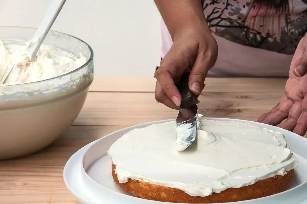 Mani esperte spalmano una soffice crema al burro su una torta.