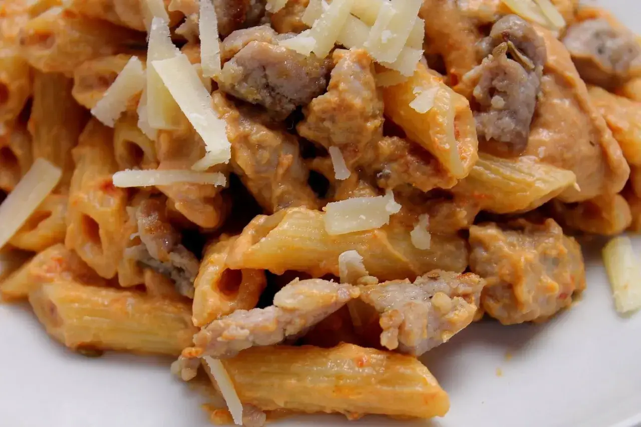 Penne cremose con salsiccia e melanzane, guarnite con scaglie di parmigiano. Un piatto ricco e saporito.