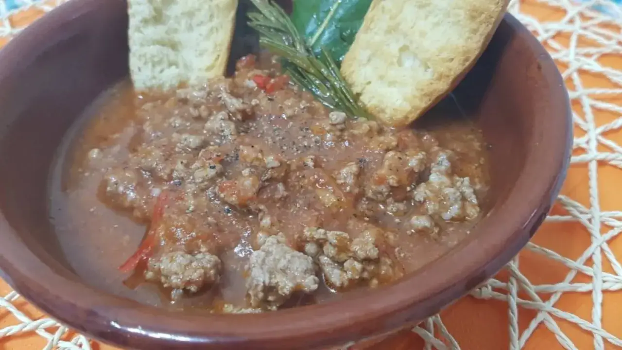 Un saporito sugo con macinato veloce, servito in una ciotola di terracotta con crostini di pane e un rametto di rosmarino.