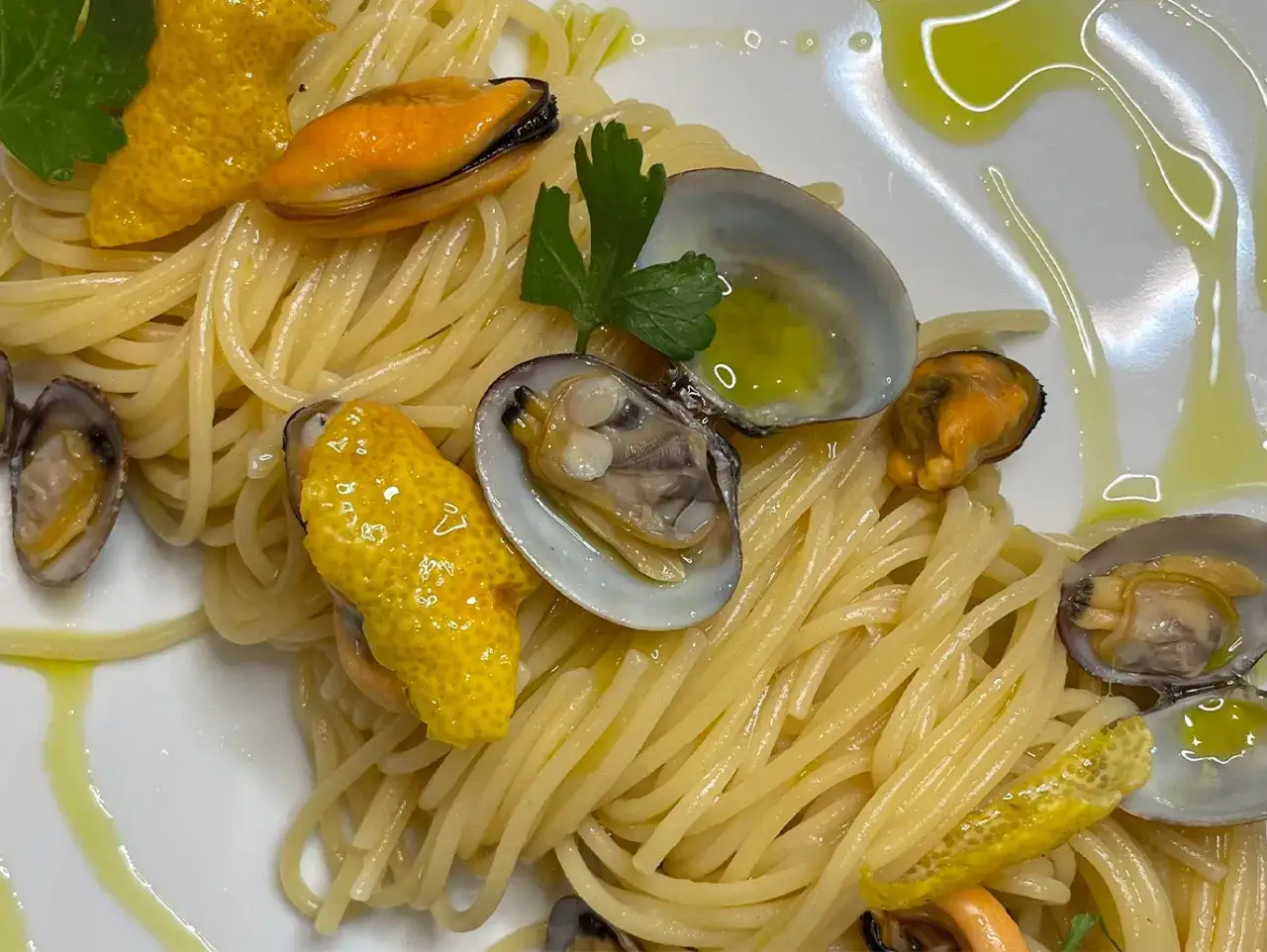 Spaghetti con cozze e vongole, un piatto cremoso e profumato, arricchito da scorze di limone e prezzemolo fresco.