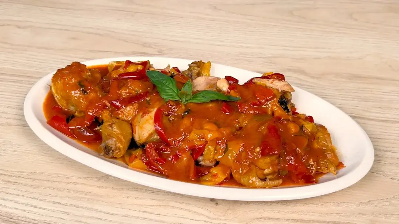 Pollo e peperoni in padella, un piatto succulento con pezzi di pollo e peperoni rossi e gialli in una salsa saporita, guarnito con basilico fresco.