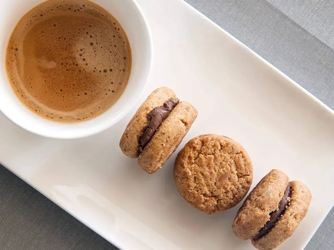 Deliziosi baci di dama con crema al cioccolato, accompagnati da un caff&egrave; espresso su un piatto bianco.