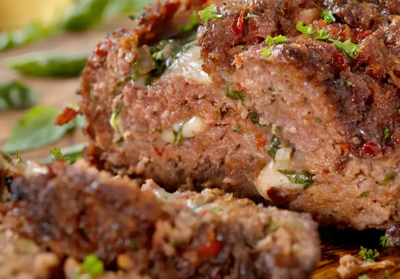 Un succulento polpettone al forno, farcito con formaggio filante e erbe aromatiche, pronto per essere gustato.