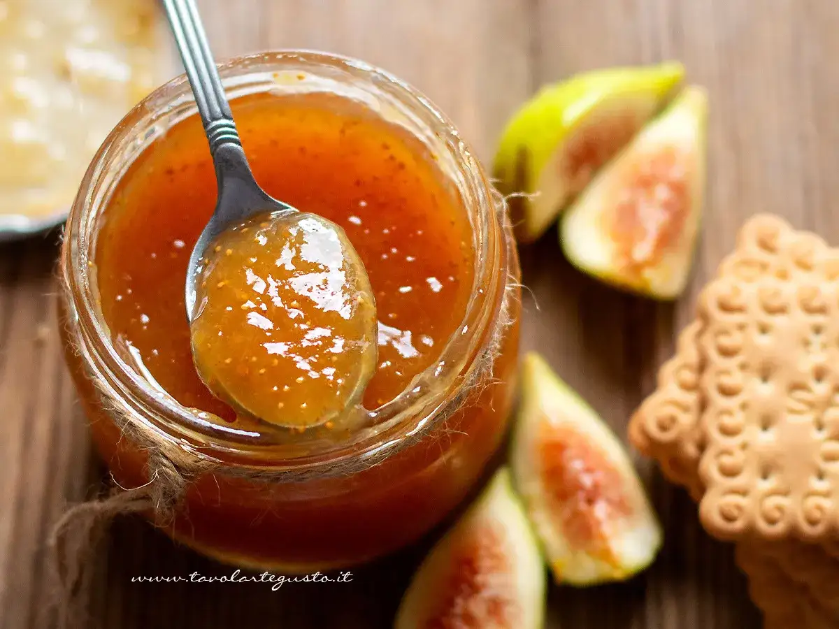 Un cucchiaio raccoglie la deliziosa marmellata di fichi da un barattolo, accanto a fichi freschi e biscotti.