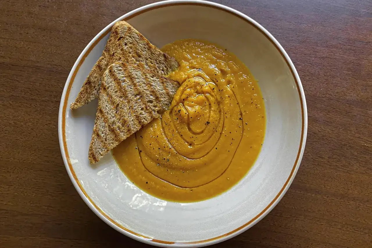 Una cremosa vellutata di zucca, guarnita con pepe nero e accompagnata da croccanti fette di pane tostato.