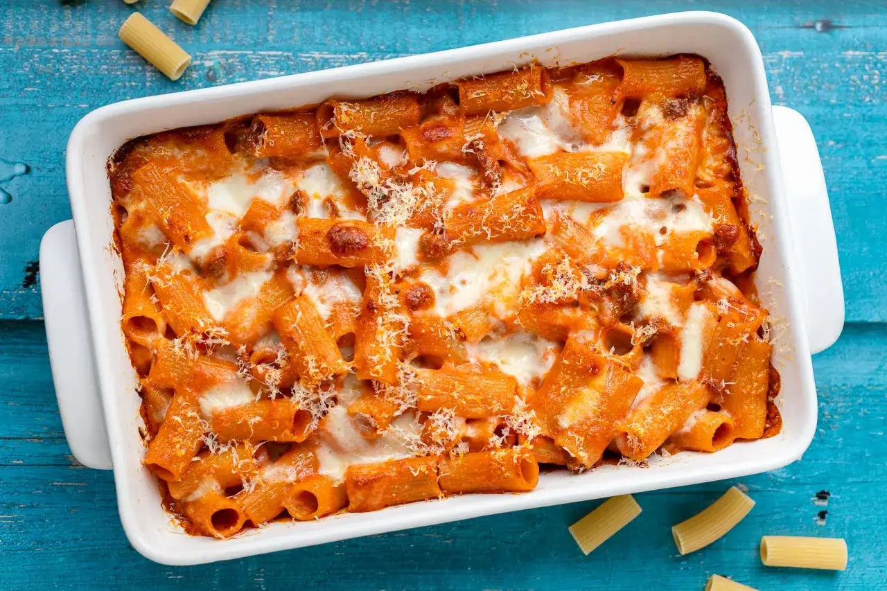 Piatto fumante di ziti al forno, ricoperti di sugo rosso e formaggio filante, pronti per essere gustati.