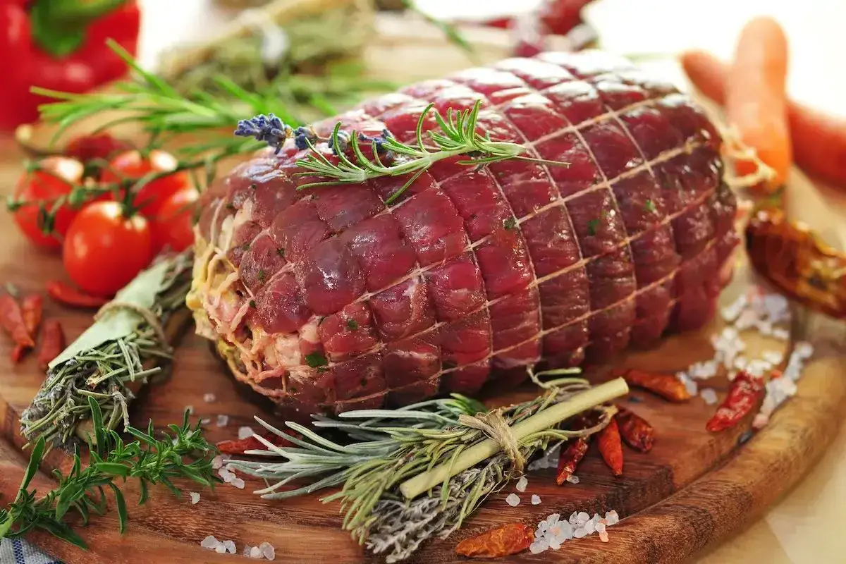 Un succulento roast beef al forno, pronto per essere cucinato con erbe aromatiche, pomodorini e peperoncini.