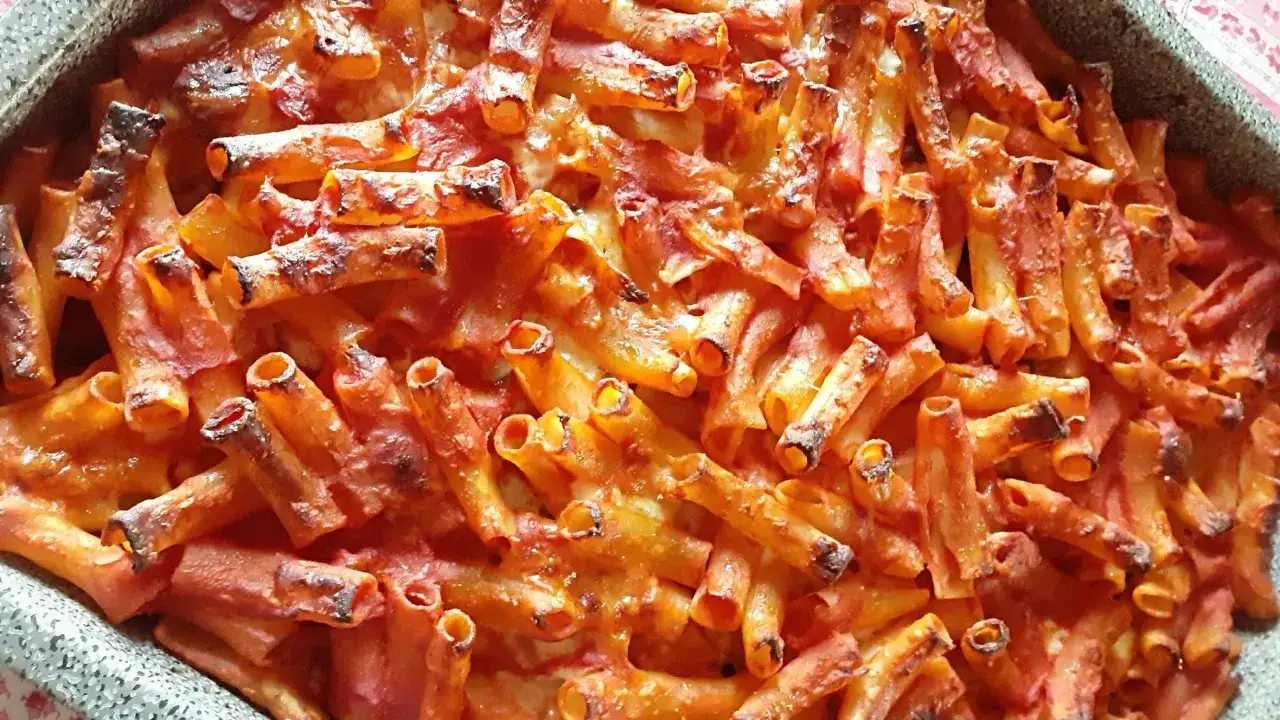 Un invitante piatto di pasta alla norma al forno, con maccheroni ricoperti di sugo rosso e formaggio fuso, leggermente abbrustoliti.