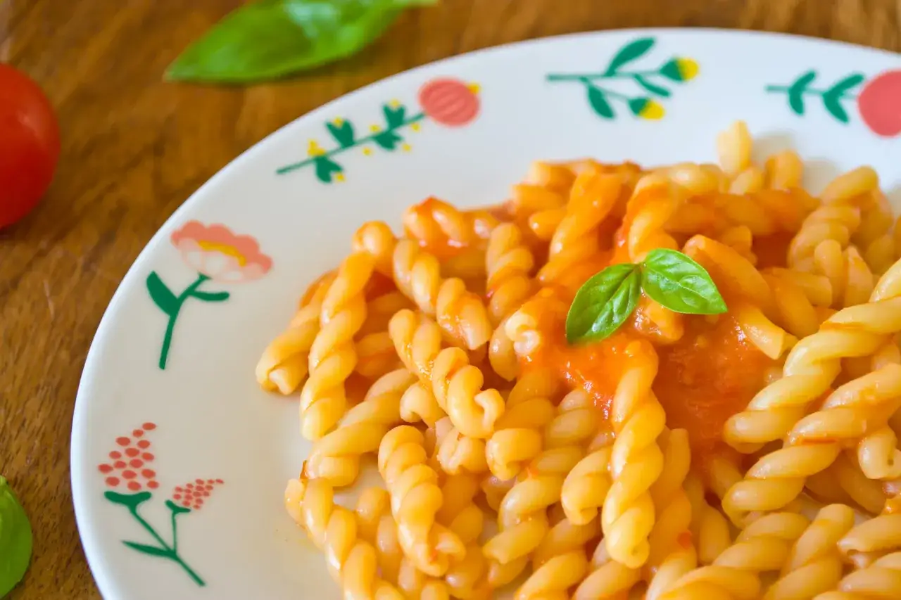 Un piatto di pasta con i pomodorini, condita con un sugo rosso e guarnita con una foglia di basilico fresco.