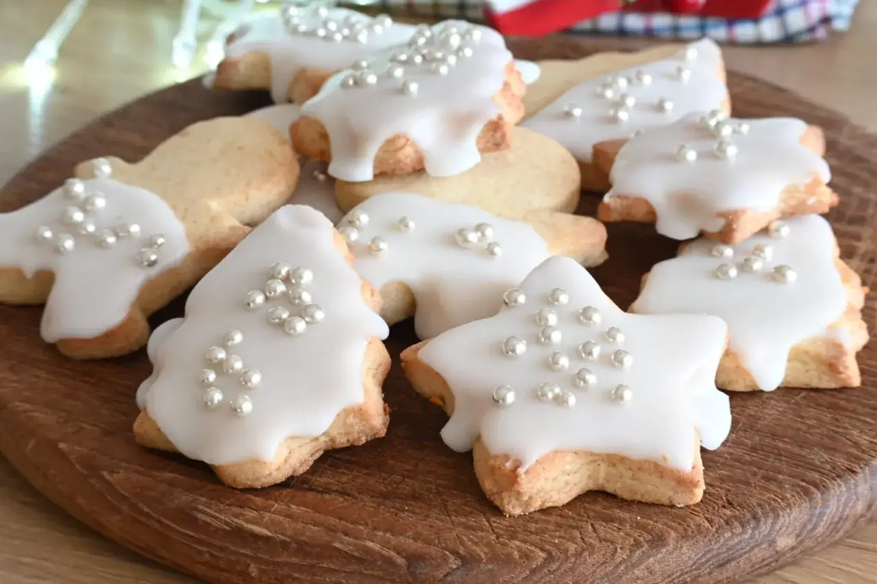Biscotti natalizi a forma di stella e albero, decorati con glassa bianca e perline argentate. La glassa per biscotti che si asciuga subito li rende perfetti per le feste.