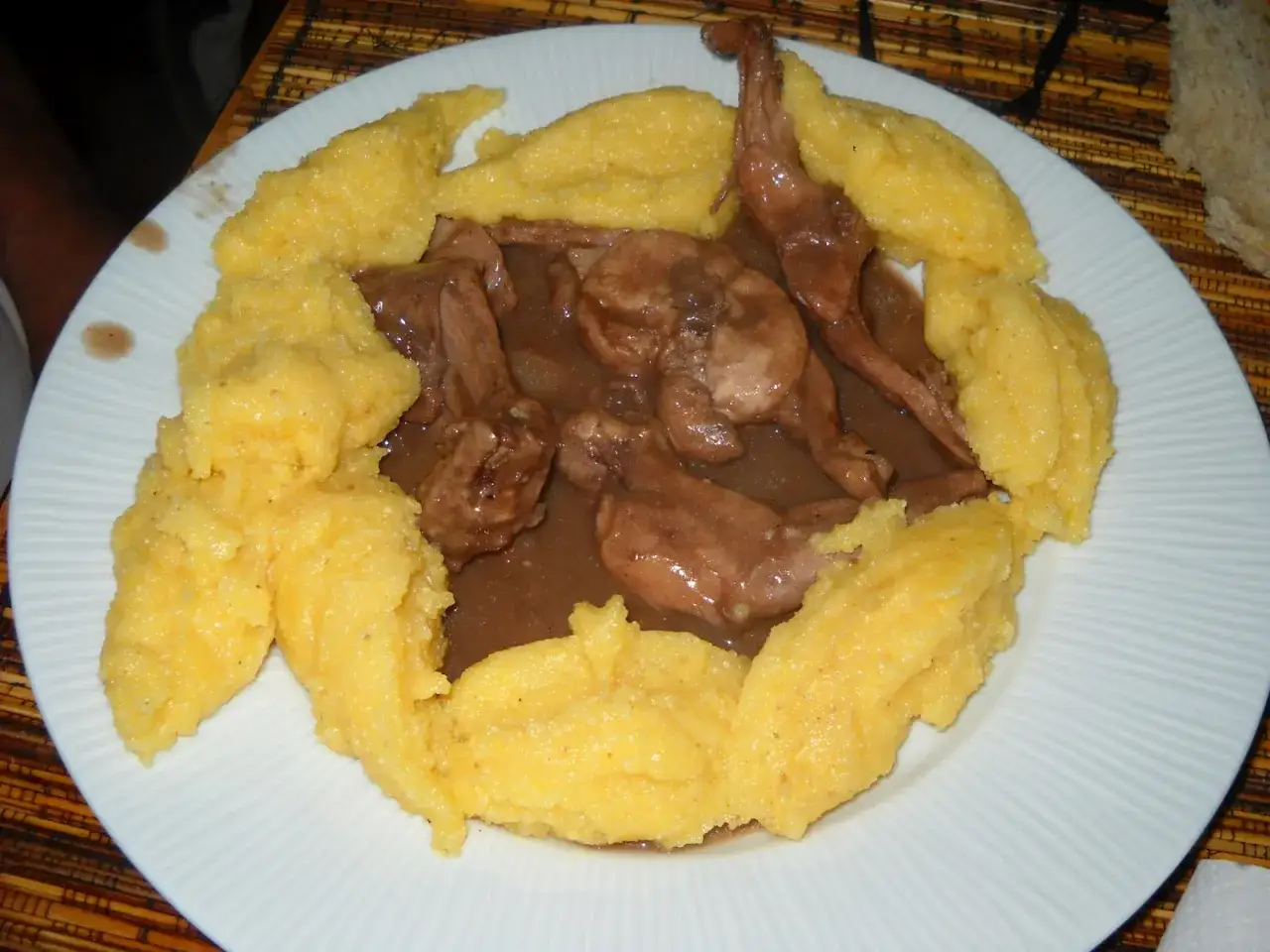 Piatto di coniglio in bianco con polenta gialla. Un classico della cucina tradizionale, servito su un piatto bianco con un contorno di pane.