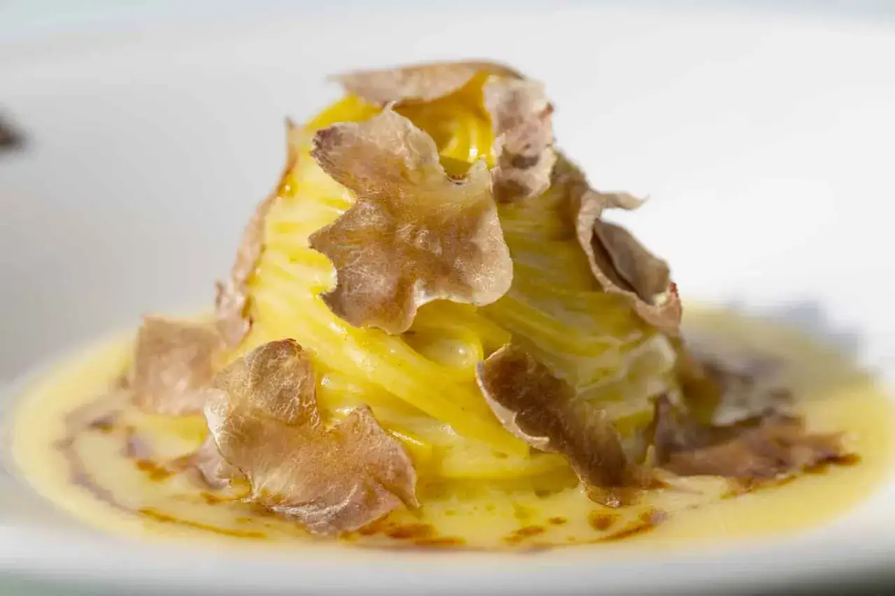 Un nido di tagliolini al tartufo cremosi, guarnito con scaglie sottili di tartufo fresco.