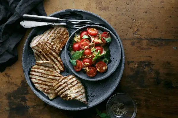 Delizioso paillard di vitello grigliato servito con un'insalata fresca di pomodorini, basilico e pinoli.