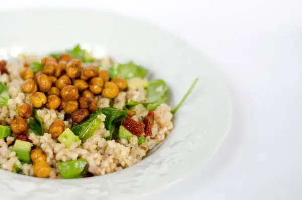 Un piatto di cous cous estivo con ceci croccanti, avocado, pomodori secchi e verdure fresche.