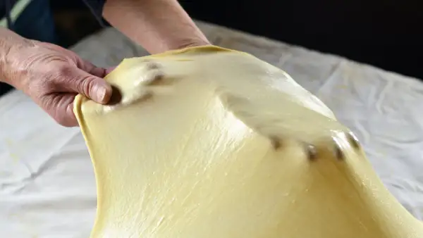 Mani che stendono la pasta matta, seguendo la ricetta originale. La pasta è sottile e traslucida, con le dita che la modellano.