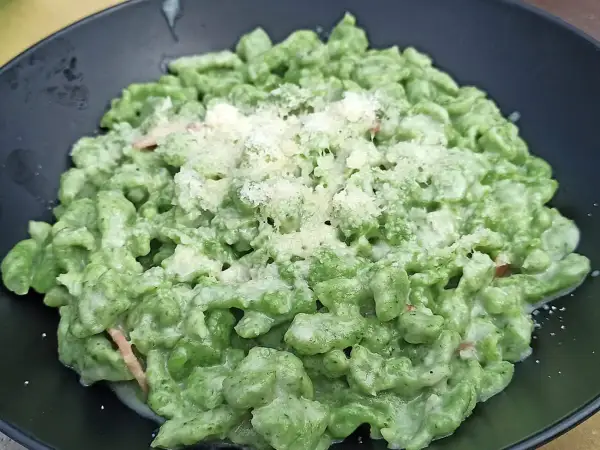 Spätzle alla tirolese verdi, conditi con panna e parmigiano, serviti in un piatto nero.
