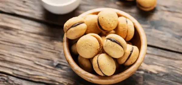 Baci di dama, deliziosi biscotti con ripieno di cioccolato, in una ciotola di legno su un tavolo rustico.