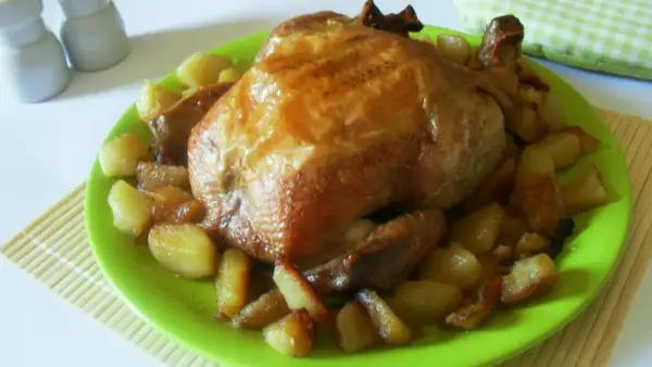 Un succulento pollo allo spiedo dorato, servito su un piatto verde brillante con patate arrosto.