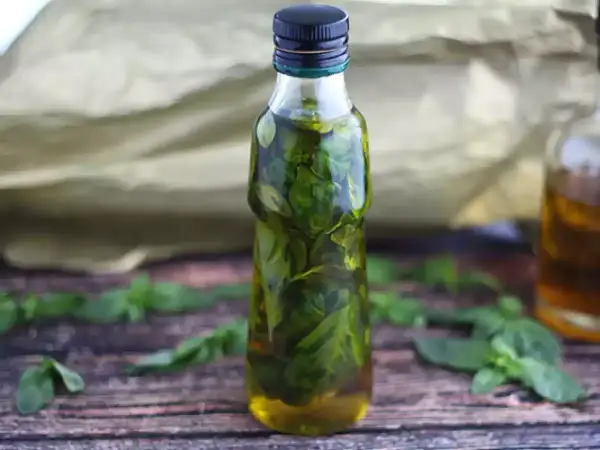 Olio al basilico fatto in casa da Benedetta, profumato e verde brillante, in una bottiglia su un tavolo di legno.