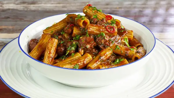Rigatoni conditi con un saporito ragù di polpo, guarniti con prezzemolo fresco e peperoncino.