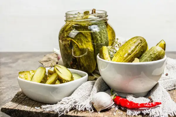 Cetrioli in agrodolce in un barattolo di vetro e in ciotole, con aglio e peperoncino.