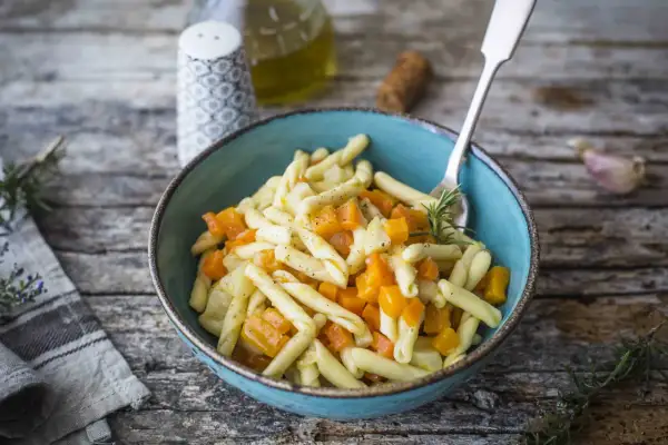Piatto di pasta con un saporito ragù di verdure, zucca e rosmarino, servito in una ciotola blu su un tavolo di legno rustico.