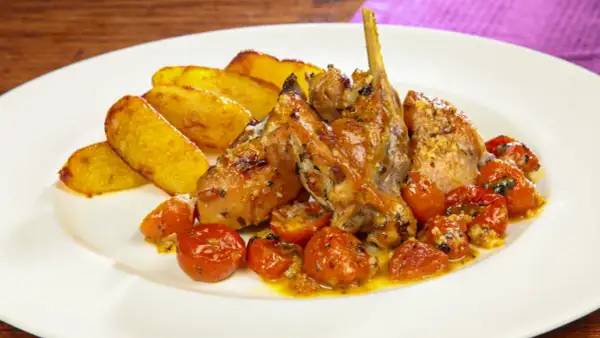 Delizioso coniglio al forno con patate arrosto e pomodorini confit, un piatto succulento e saporito.