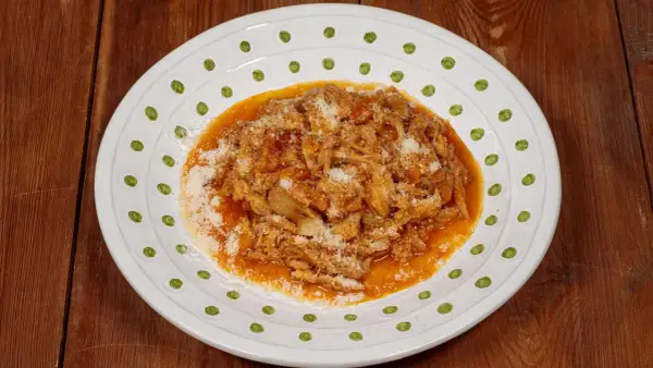 Un piatto di trippa alla fiorentina, ricca e saporita, cosparsa di parmigiano, servita su un piatto bianco decorato.
