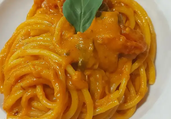 Un piatto invitante di pasta con i pomodorini, condita con una salsa cremosa e guarnita con una foglia di basilico fresco.