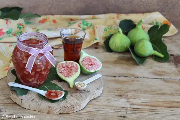 Un vasetto di marmellata di fichi, con fichi freschi, un bicchierino di liquore e un cucchiaino con la marmellata.