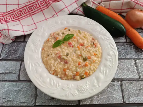 Un cremoso risotto con verdure, guarnito con basilico fresco. Accanto, carote, zucchine e cipolla, ingredienti per un piatto gustoso.