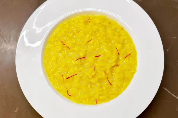 Un cremoso risotto alla milanese, giallo intenso con fili di zafferano, servito in un piatto bianco.