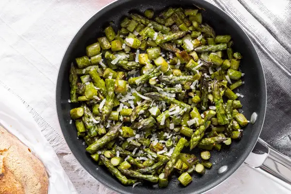 Asparagi verdi in padella, saltati e cosparsi di parmigiano grattugiato, pronti per essere gustati.