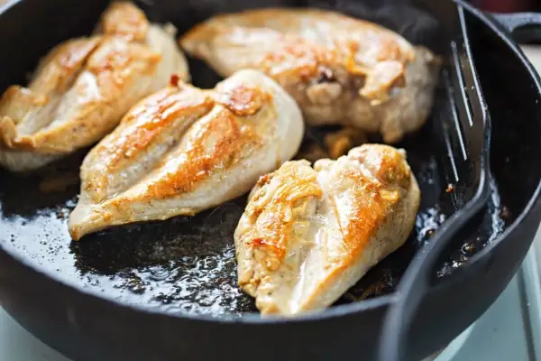 Petto di pollo dorato e succulento che sfrigola in padella, pronto per essere gustato.