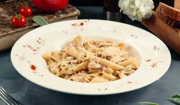 Piatto di pasta del pastore con crema, pollo e formaggio grattugiato, guarnito con paprika.