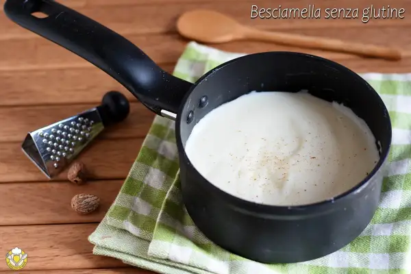 Besciamella senza glutine cremosa in pentolino, con noce moscata grattugiata. Accanto, noce moscata intera e una grattugia.