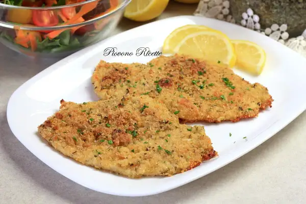 Due cotolette di pollo al forno dorate e croccanti, guarnite con prezzemolo fresco e servite con spicchi di limone e un'insalata mista.