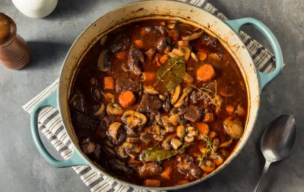 Un invitante spezzatino con funghi, carote e erbe aromatiche in una casseruola blu.