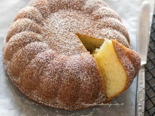 Torta 7 vasetti soffice e dorata, cosparsa di zucchero a velo. Una fetta è stata tagliata, rivelando l'interno profumato.