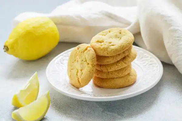 Biscotti senza burro al limone, dorati e fragranti, su un piatto bianco, con limoni freschi a lato.