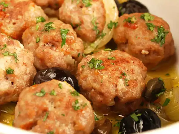 Polpette di carne succulente, dorate e profumate, servite con olive nere e un contorno di verdure.
