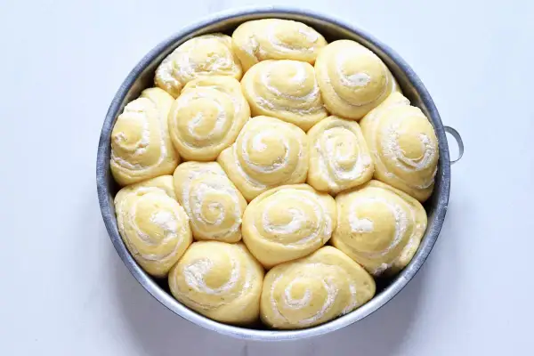 Torta di rose lievitata, pronta per essere infornata, con soffici spirali di pasta e una spolverata di zucchero a velo.