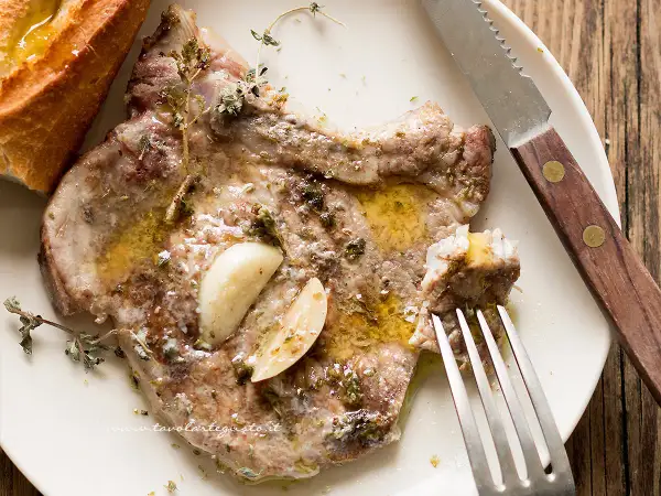 Succulenta braciola di maiale condita con aglio e erbe aromatiche, servita con pane croccante.