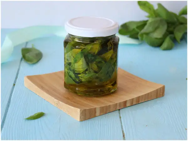 Un barattolo di olio al basilico fatto in casa, con foglie fresche immerse nell'olio dorato, su un tagliere di legno.